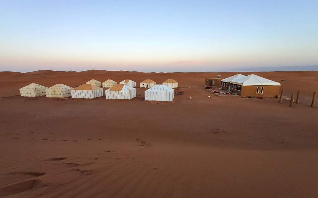 Desert camp with white nomad tents surrounded by sand dunes at dusk