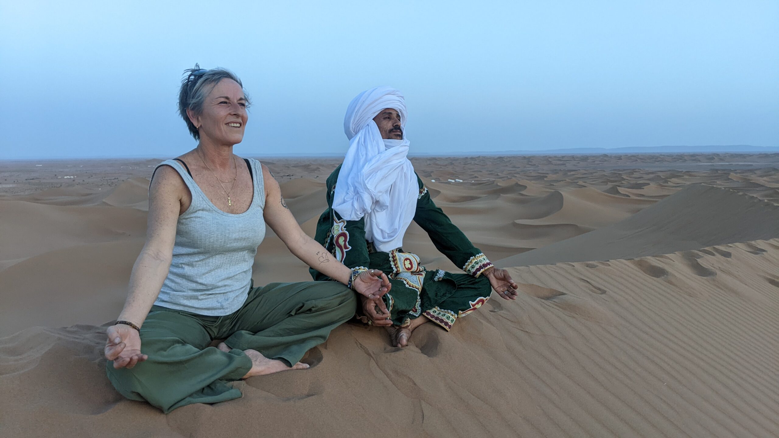 Two people meditating together on a Sahara dune at dusk