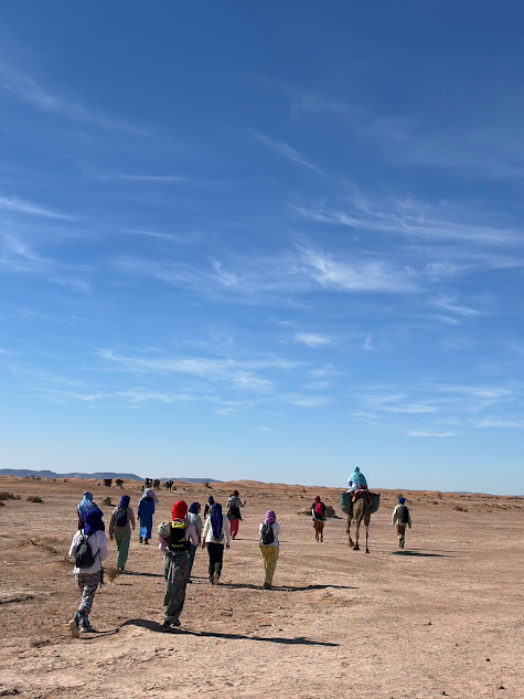 Group trekking across a wide desert plain with a camel under a bright blue sky