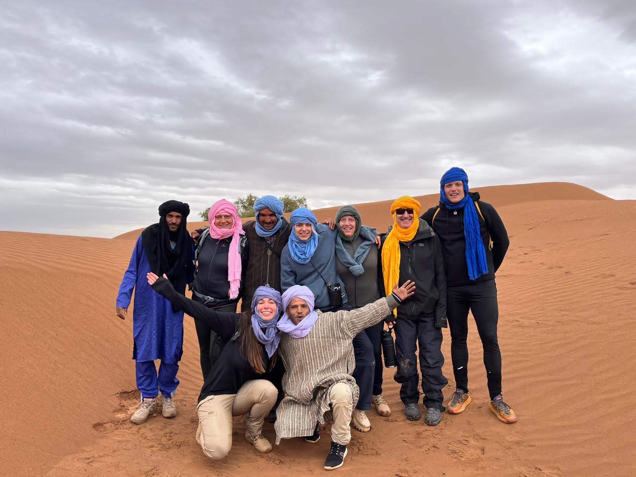 Group of travelers and local guides posing together on golden sand dunes