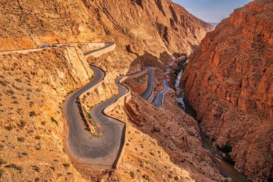 Winding mountain road through a dramatic red-rock canyon with a river below