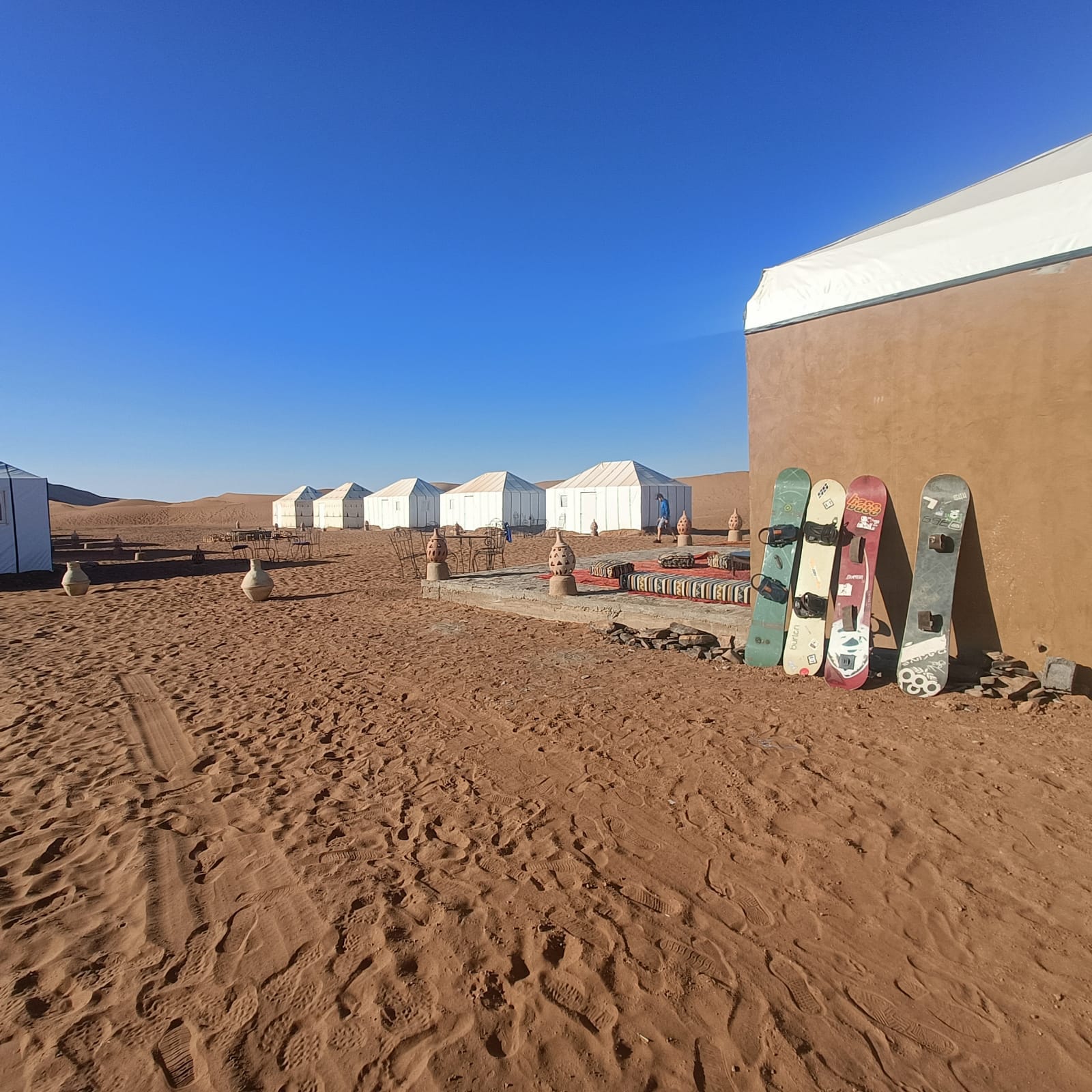 Desert camp with white tents and sandboards leaning against a building