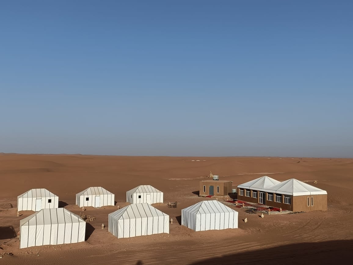 Desert camp with white tents and a main building set among wide sand dunes