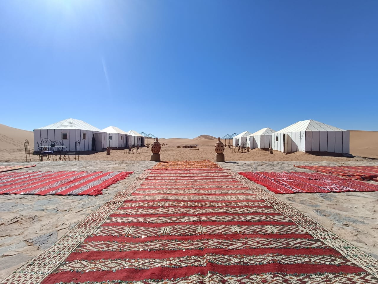 Rows of white desert tents with red patterned carpets laid across the sand