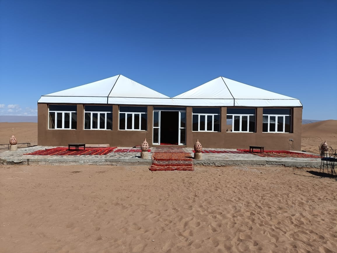 Desert camp building with white tent-style roofs surrounded by sand