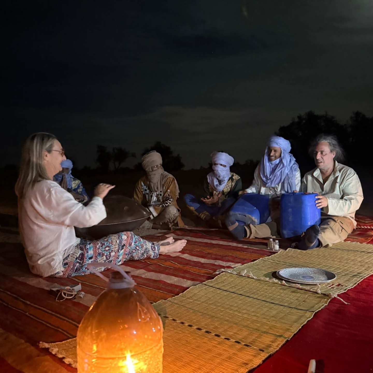 Travelers and local hosts sitting together on carpets at night in a desert camp
