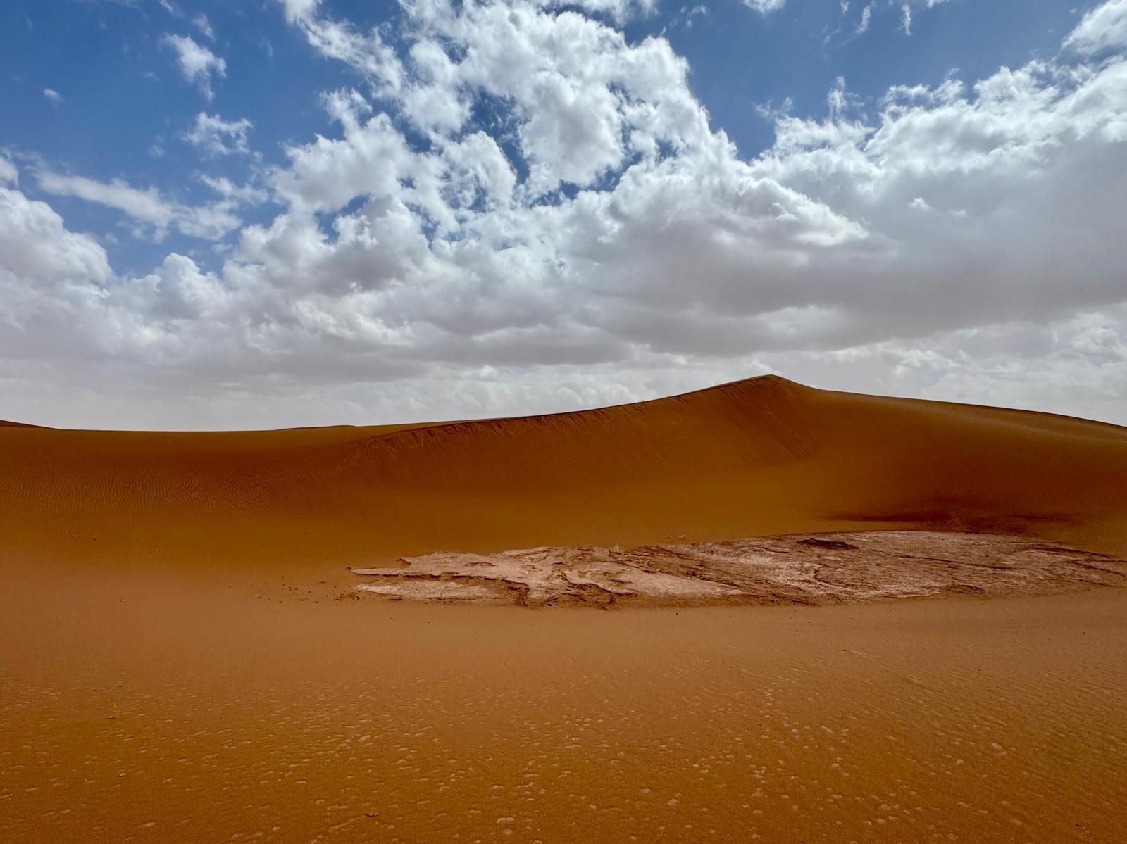 Large golden sand dune beneath dramatic white clouds and blue sky