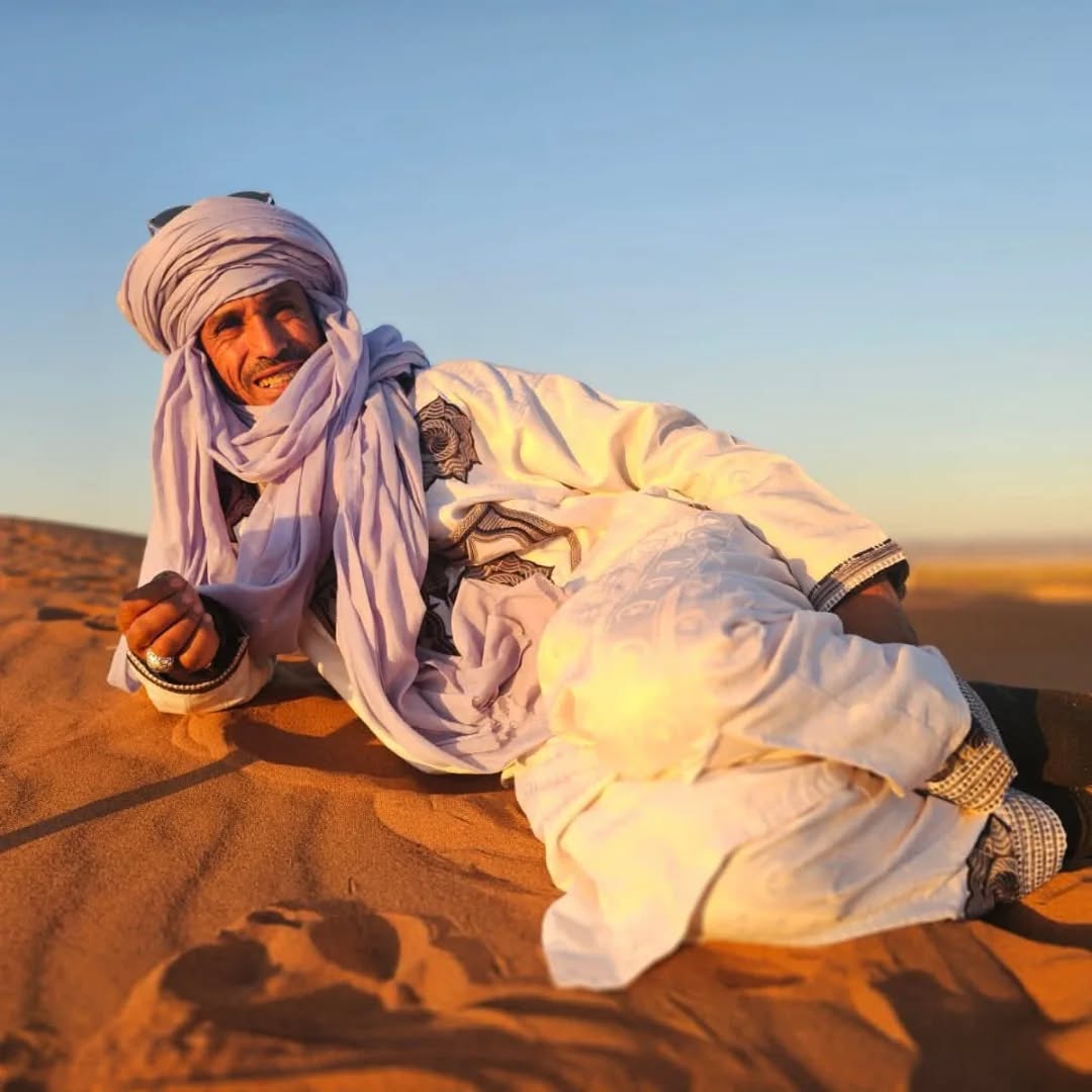 Man in traditional desert clothing reclining on a sand dune at golden hour